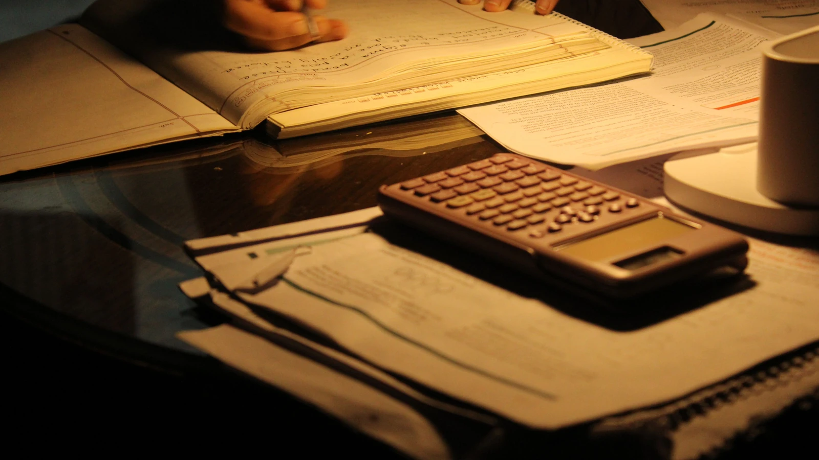 Una sessione di studio concentrata di notte, con libri aperti e una calcolatrice su un tavolo scarsamente illuminato.
