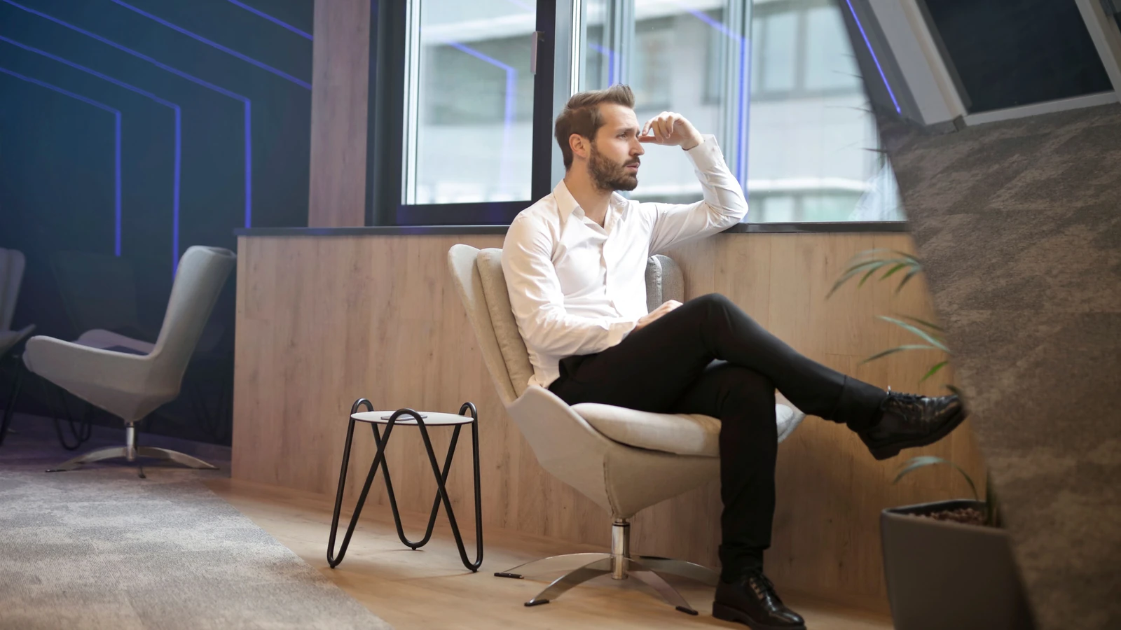 Un uomo pensieroso in un interno di ufficio moderno, seduto e che guarda fuori.