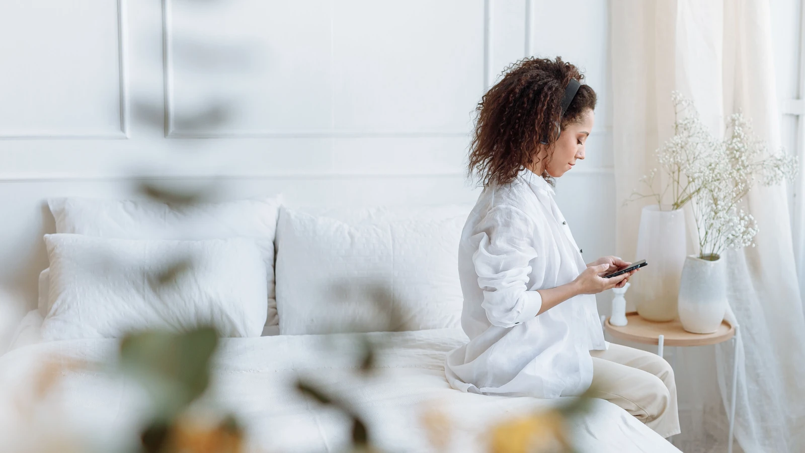 Donna seduta sul comodino che usa il cellulare con le cuffie