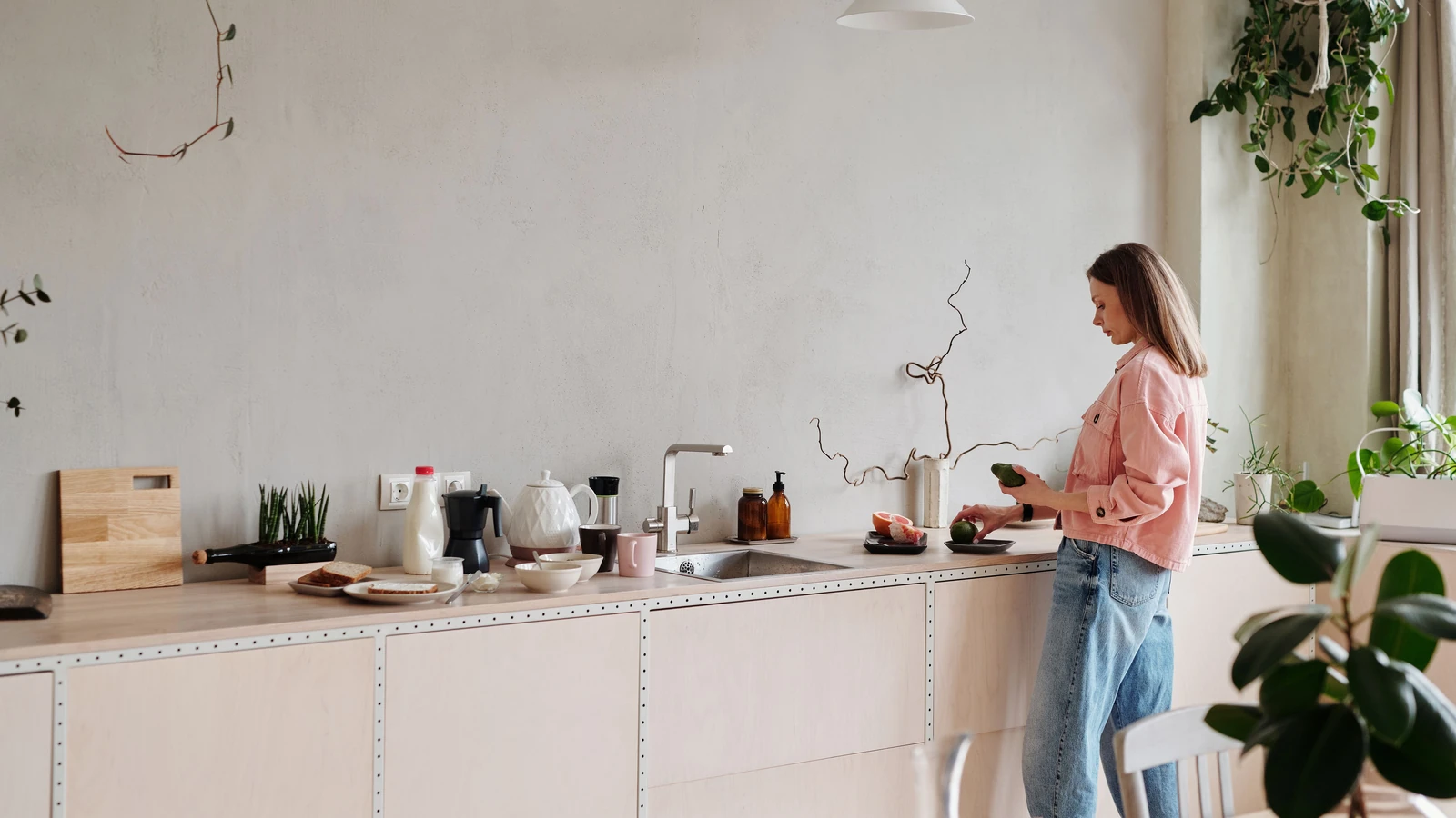 Donna che affetta avocado su un elegante piano cucina circondata da piante. Ambiente interno luminoso.