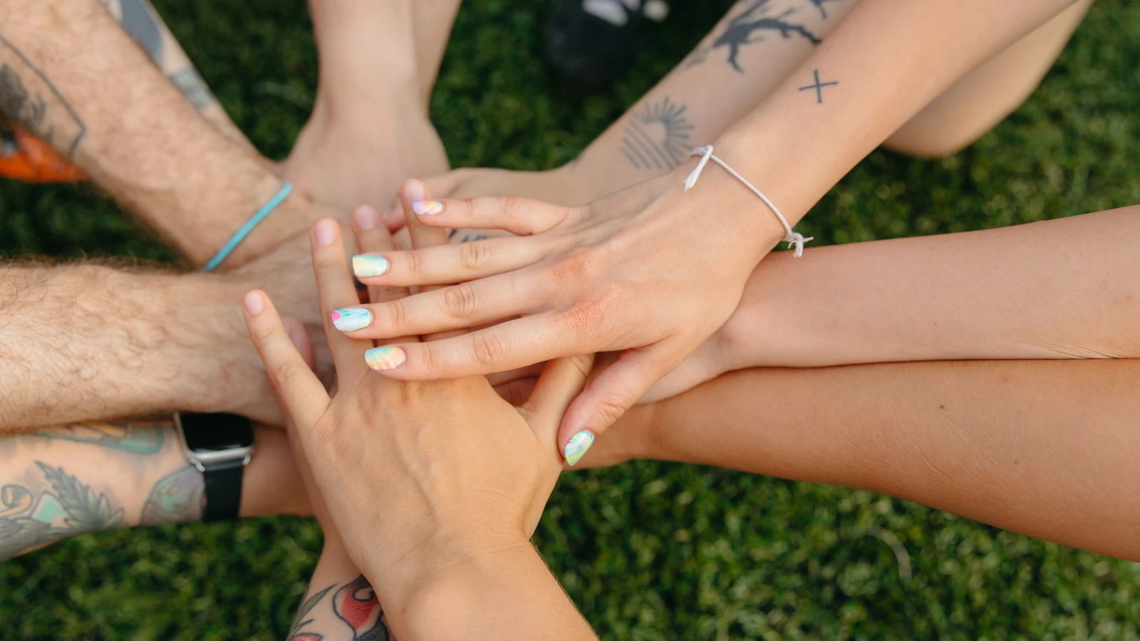 Un gruppo di mani di persone con tatuaggi e unghie colorate che simboleggiano l'unità sull'erba.