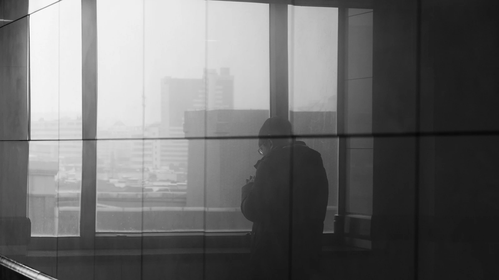 Silhouette di una persona riflessa in una finestra, con vista sulla città in bianco e nero.
