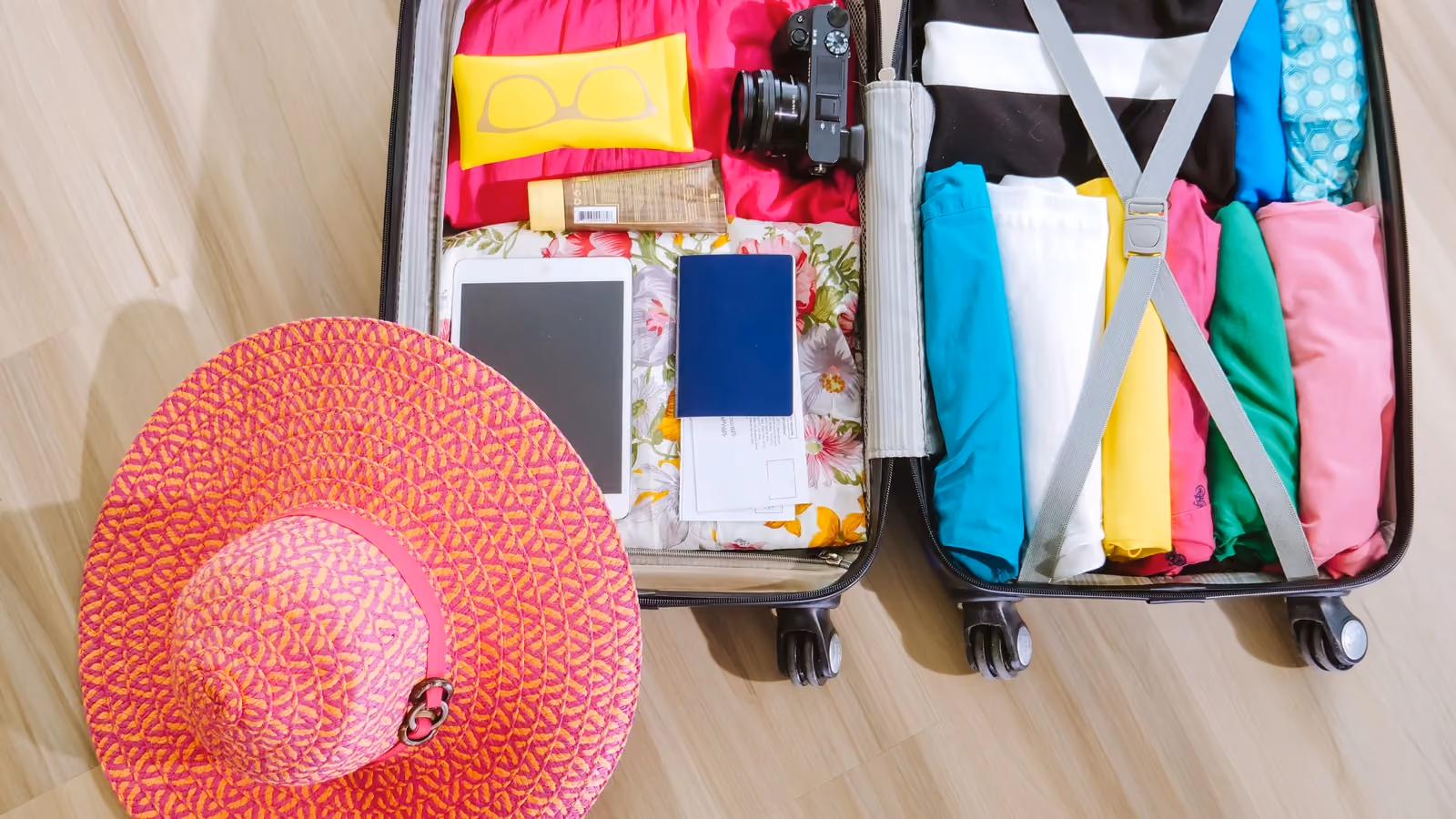 Vista dall'alto di una valigia piena di vestiti, una fotocamera e un cappello da sole, pronta per un viaggio estivo. — Kindel Media – Pexels