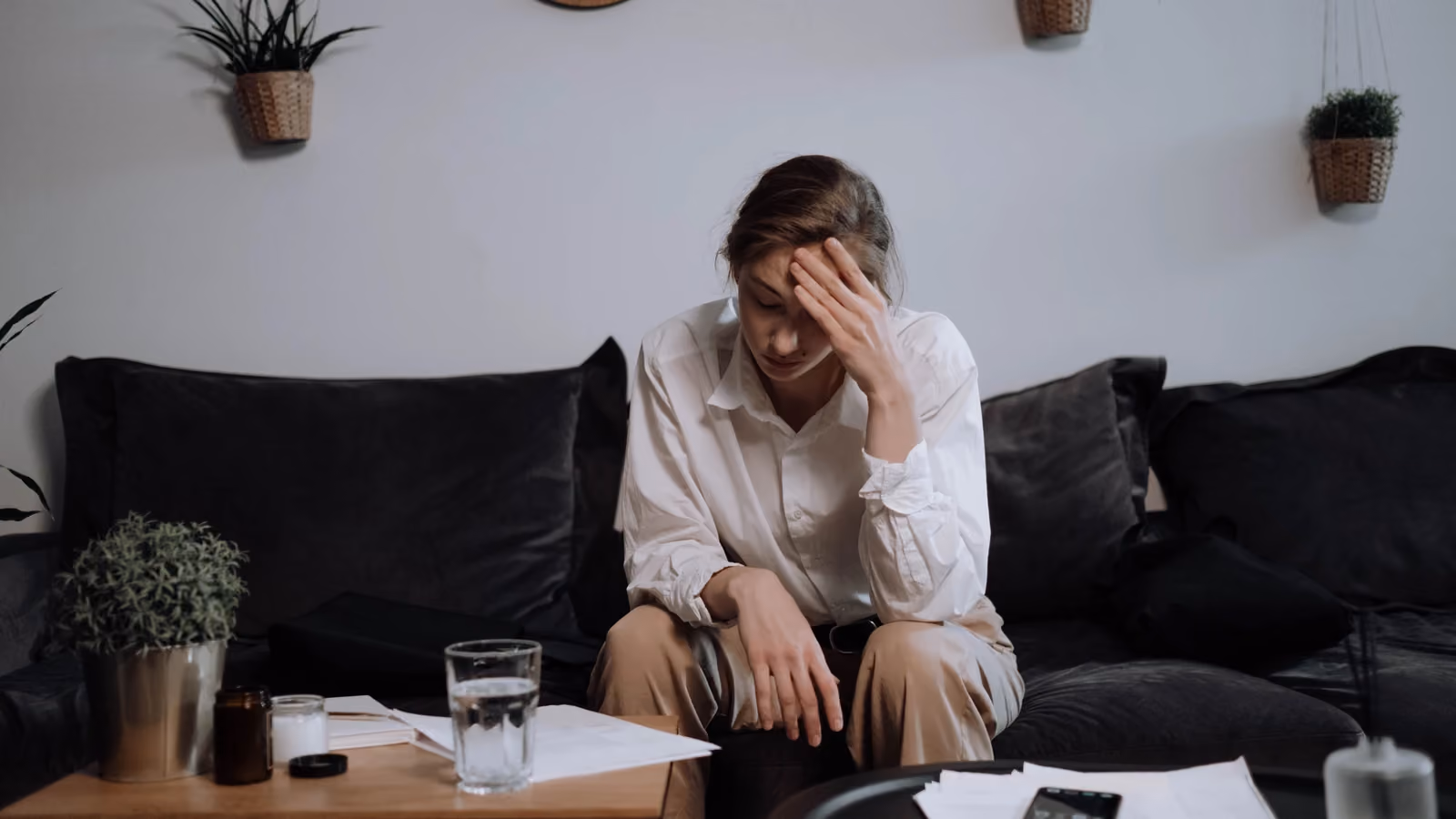 Donna che prova stress e mal di testa mentre è seduta su un divano a casa, circondata da fogli. — Ron Lach – Pexels