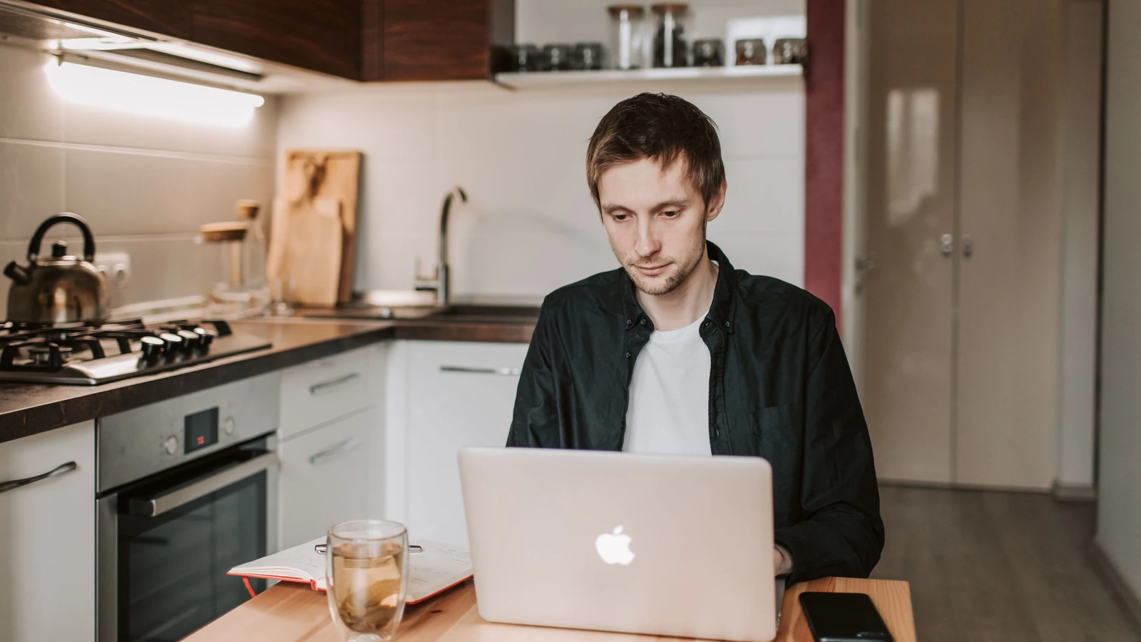 Un giovane che utilizza un laptop in una cucina accogliente, illustrando lo stile di vita del lavoro remoto.