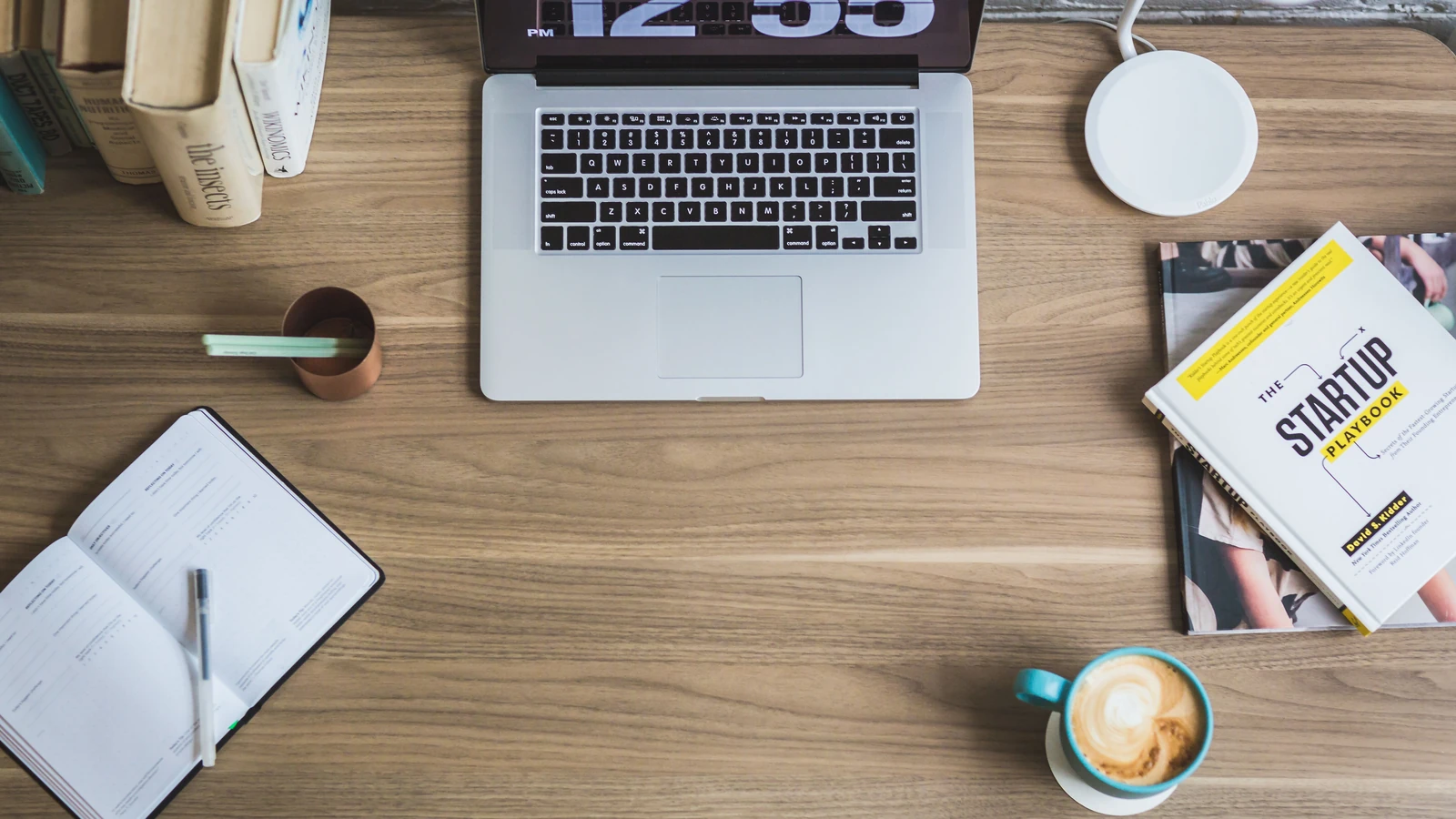 Vista dall'alto di un moderno spazio di lavoro con un laptop, tazza di caffè e libri sulle startup su una scrivania di legno.