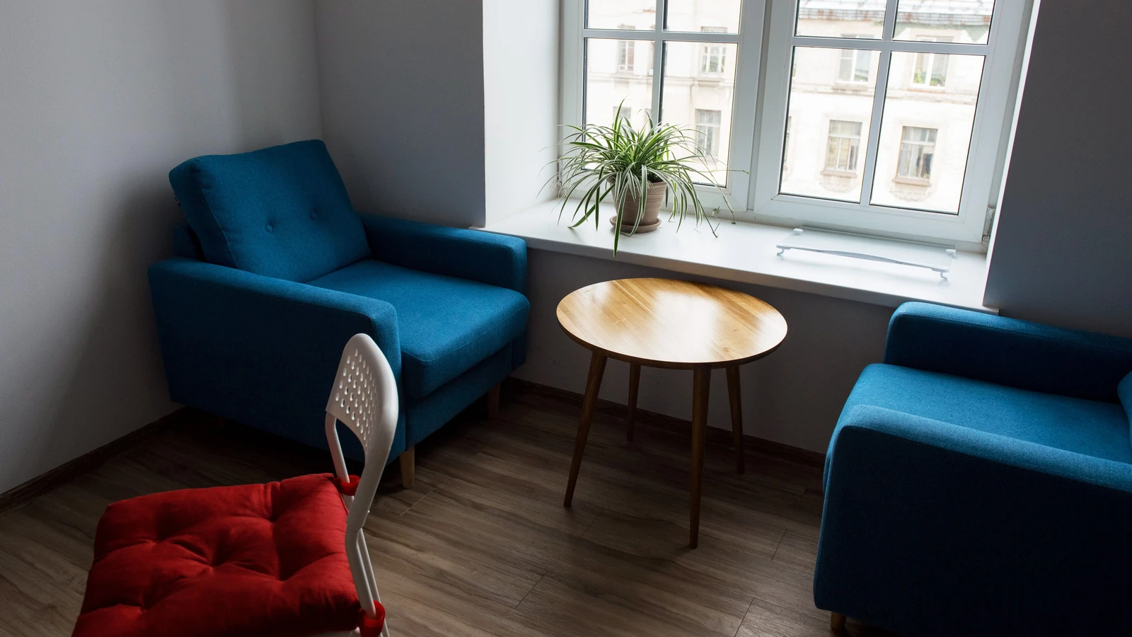 Uno spazio abitativo contemporaneo con poltrone blu, una sedia rossa e mobili in legno, ideale per rilassarsi.