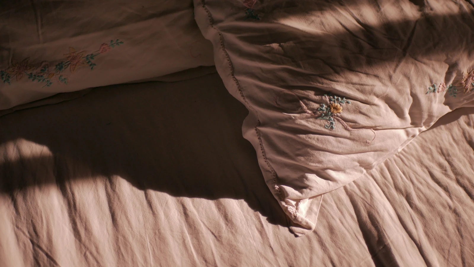 Una scena di camera da letto accogliente con luce soffusa che mette in risalto i cuscini e un lenzuolo.