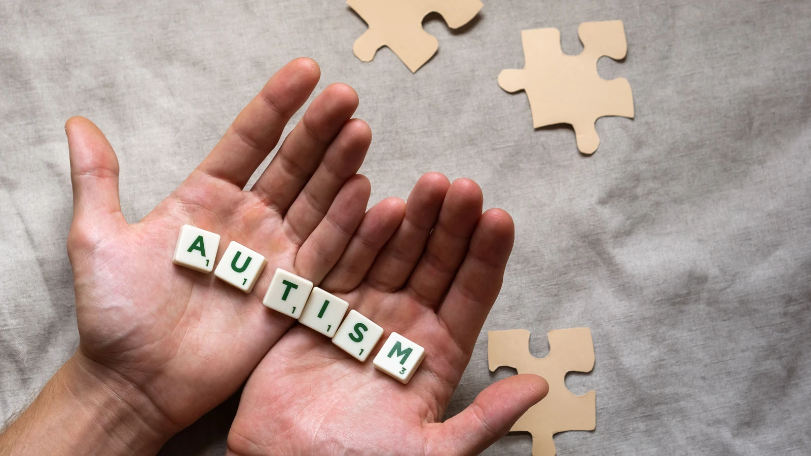 Primo piano di mani con un messaggio di sensibilizzazione sull'autismo su lettere di Scrabble e pezzi di puzzle su tessuto.