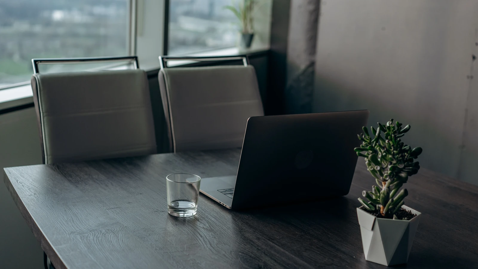 Un elegante spazio di lavoro con un laptop, un bicchiere da bere e una pianta in vaso con vista sulla città. — Mikhail Nilov – Pexels