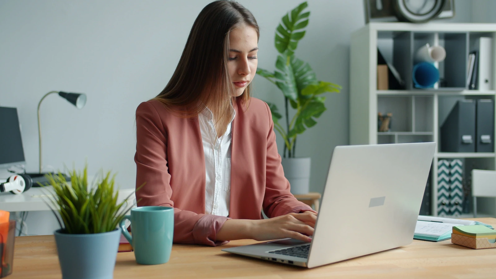 Donna giovane e sicura in abbigliamento da lavoro che utilizza il computer in un ufficio moderno.
