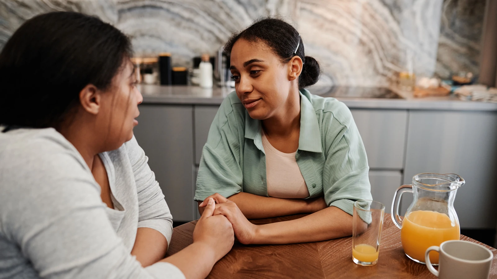 Due donne si impegnano in una conversazione di supporto durante la colazione in una cucina accogliente.