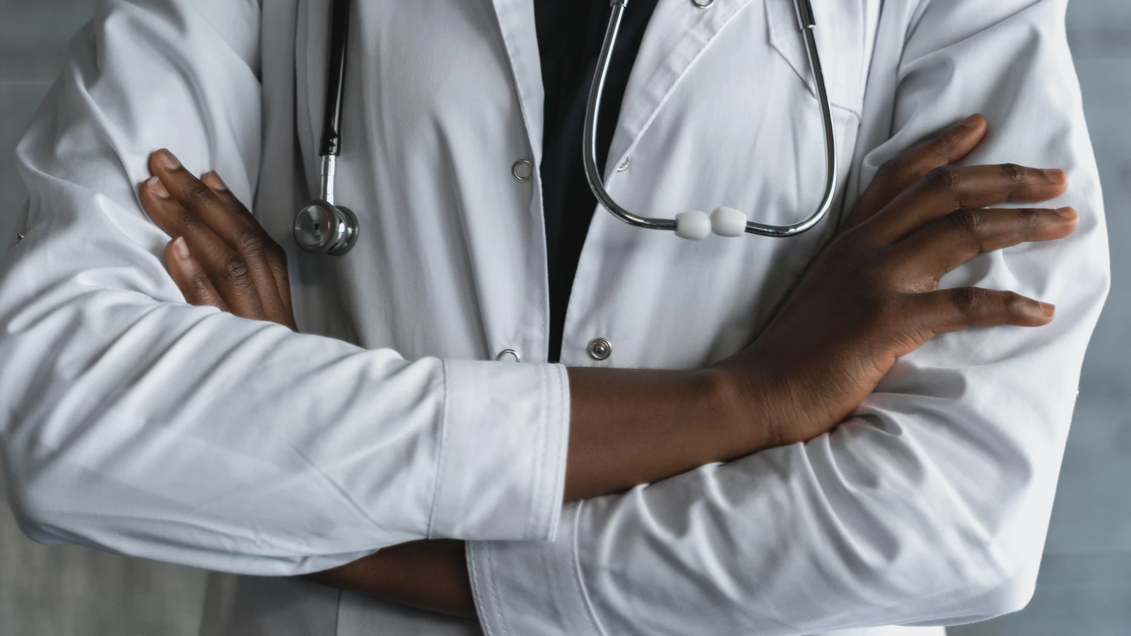 Primo piano di un medico sicuro di sé in camice da laboratorio con le braccia incrociate e stetoscopio.