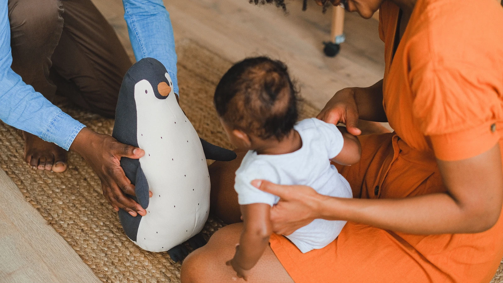 Una famiglia che gioca in casa con un bambino e un pinguino di peluche, promuovendo gioia.
