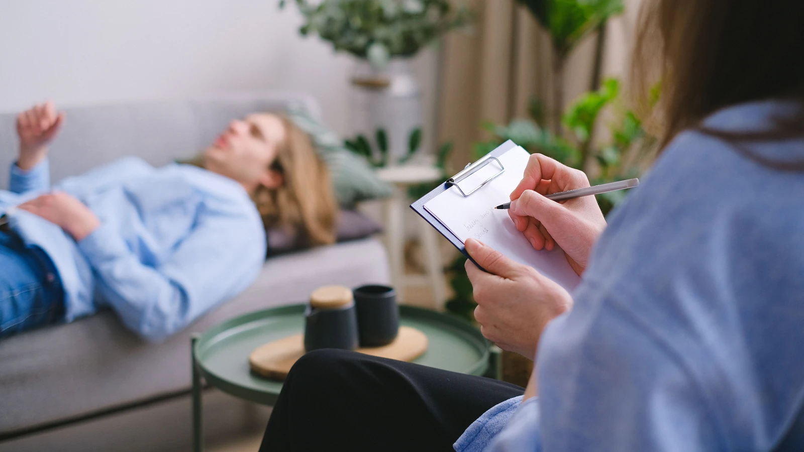 Una sessione di terapia in corso con un terapeuta che prende appunti mentre un paziente è sdraiato su un divano.