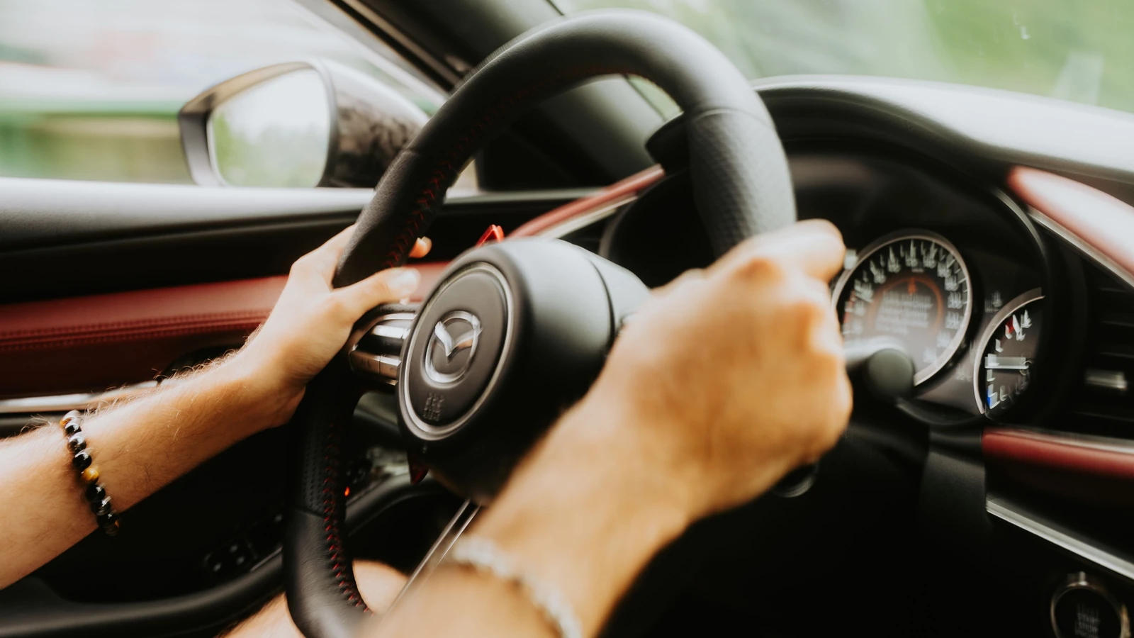 Primo piano di mani che afferrano il volante di un'auto con gli indicatori del cruscotto visibili.