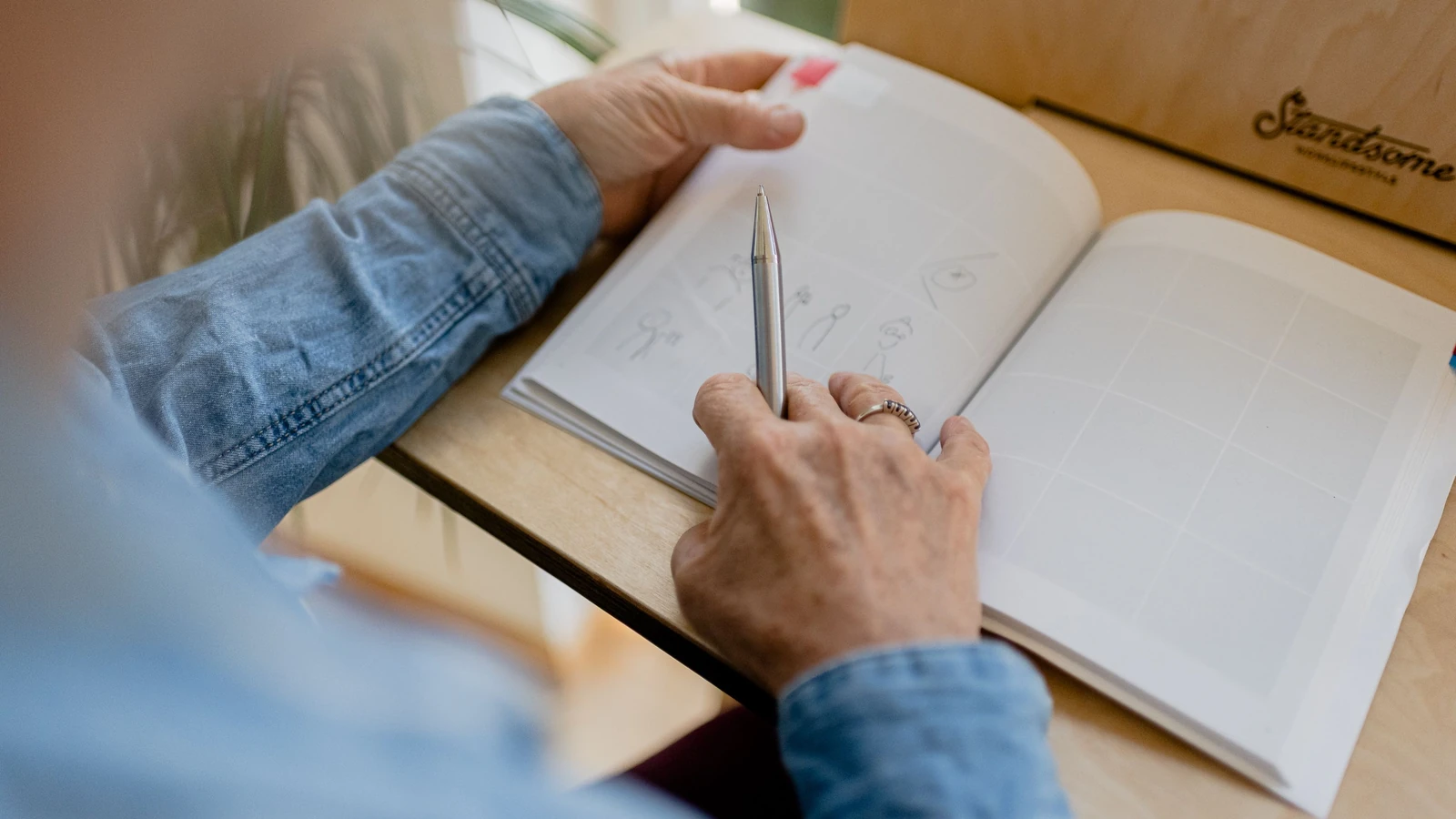 Mani che disegnano schizzi in un quaderno con una penna su un tavolo di legno. Ideale per temi creativi e educativi.