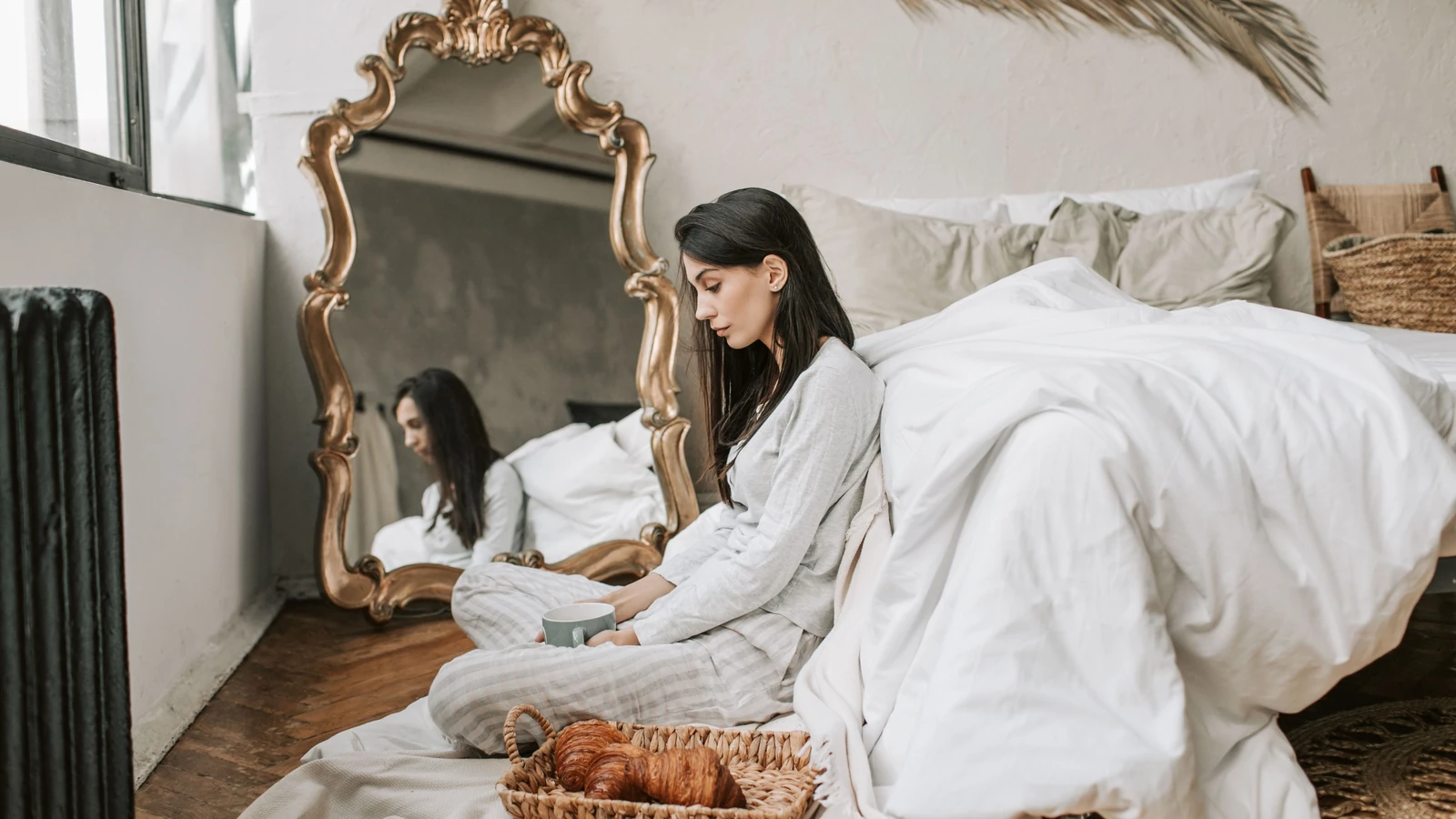 Una donna che gusta caffè e croissant in un'accogliente camera da letto con decorazioni eleganti.