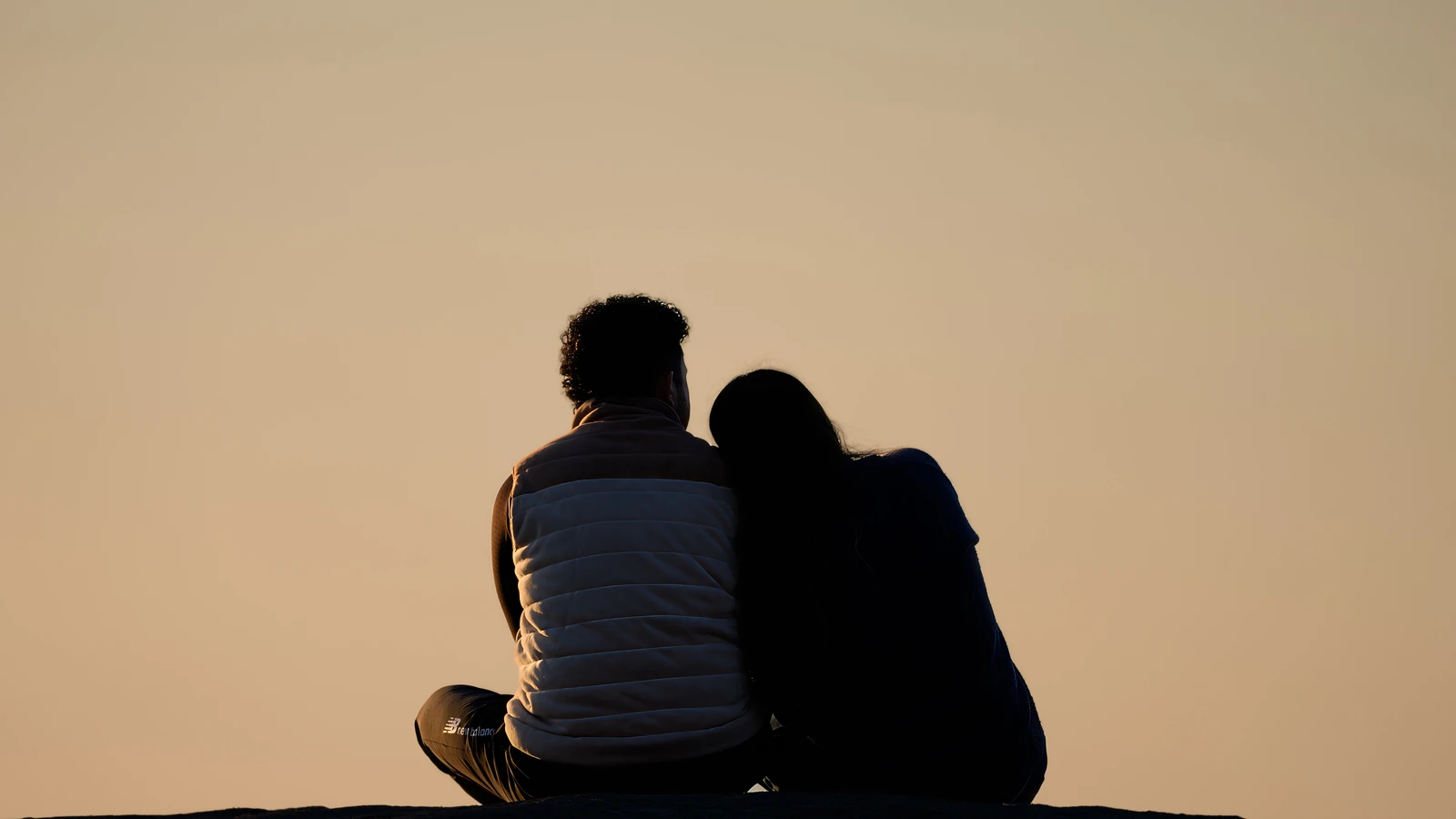 Una coppia seduta che si abbraccia mentre guarda l'alba in un parco, a simboleggiare romanticismo e pace.