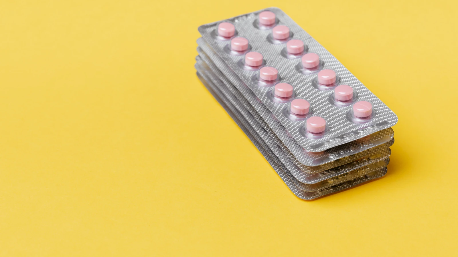 Pila di blister con pillole rosa su sfondo giallo brillante con spazio per testo
