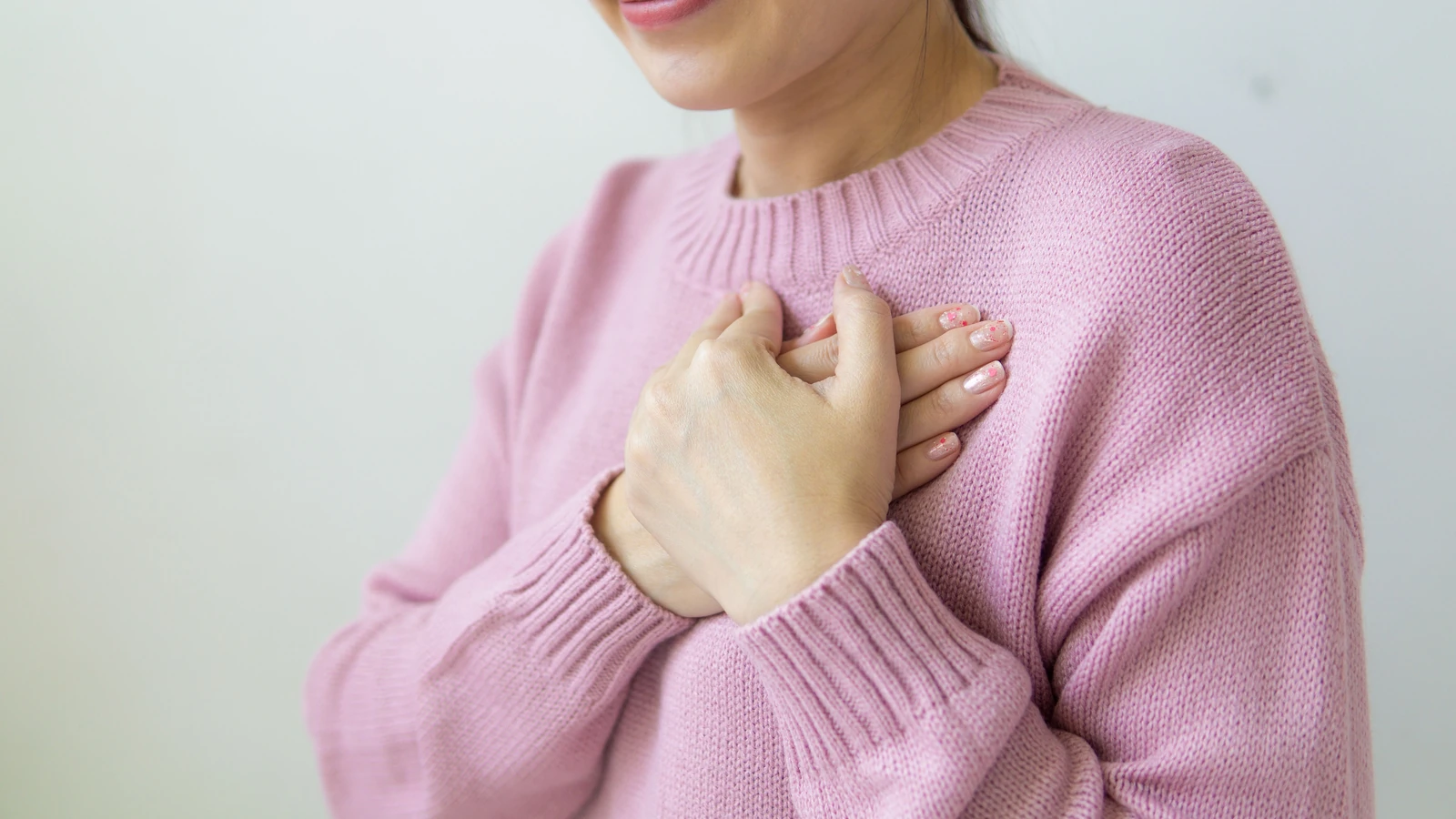 Una donna serena in un maglione rosa si tiene il petto, simboleggiando calore e cura.