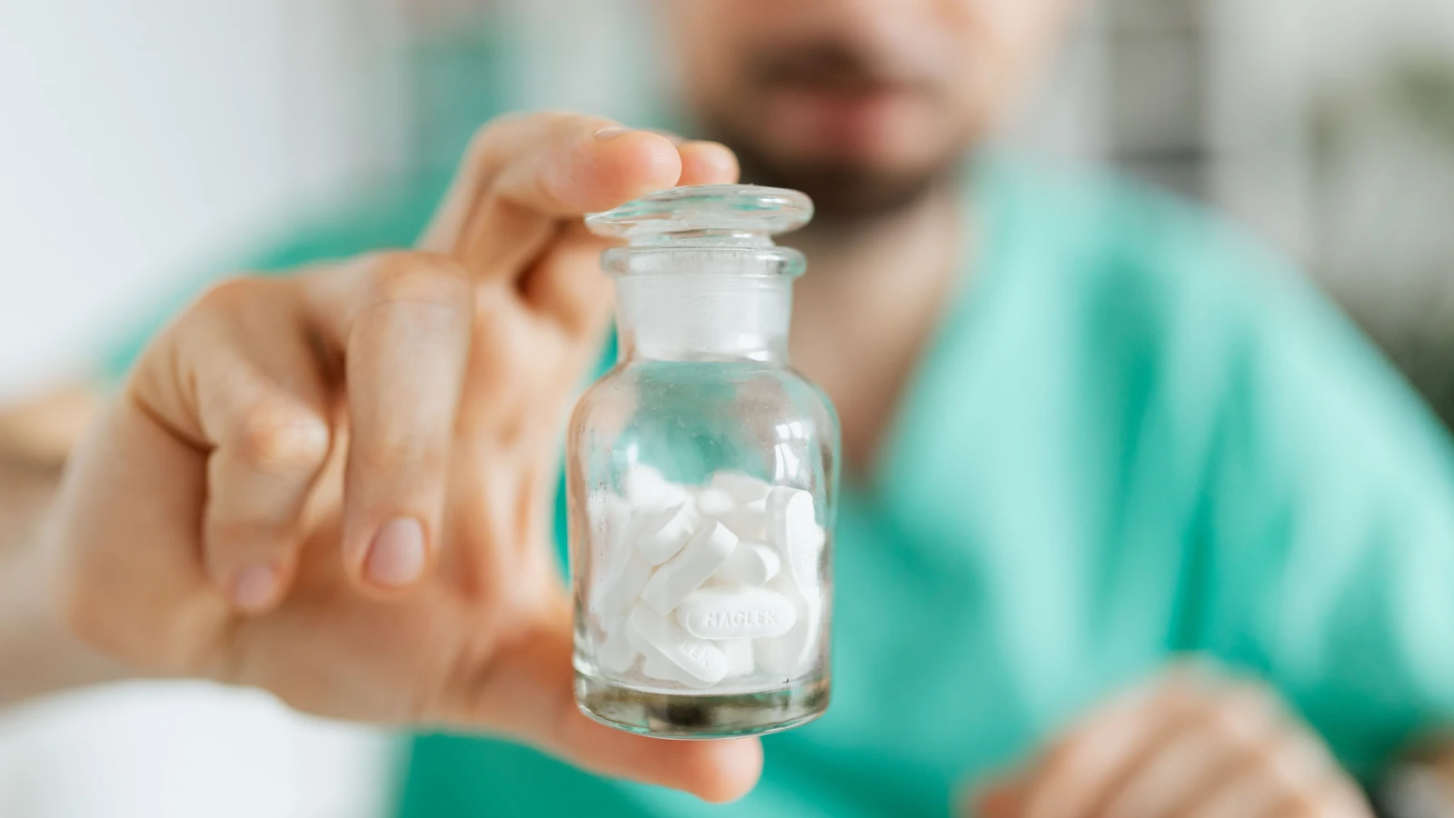 Operatore sanitario in uniforme che tiene una bottiglia di pillole, concentrandosi sul farmaco.