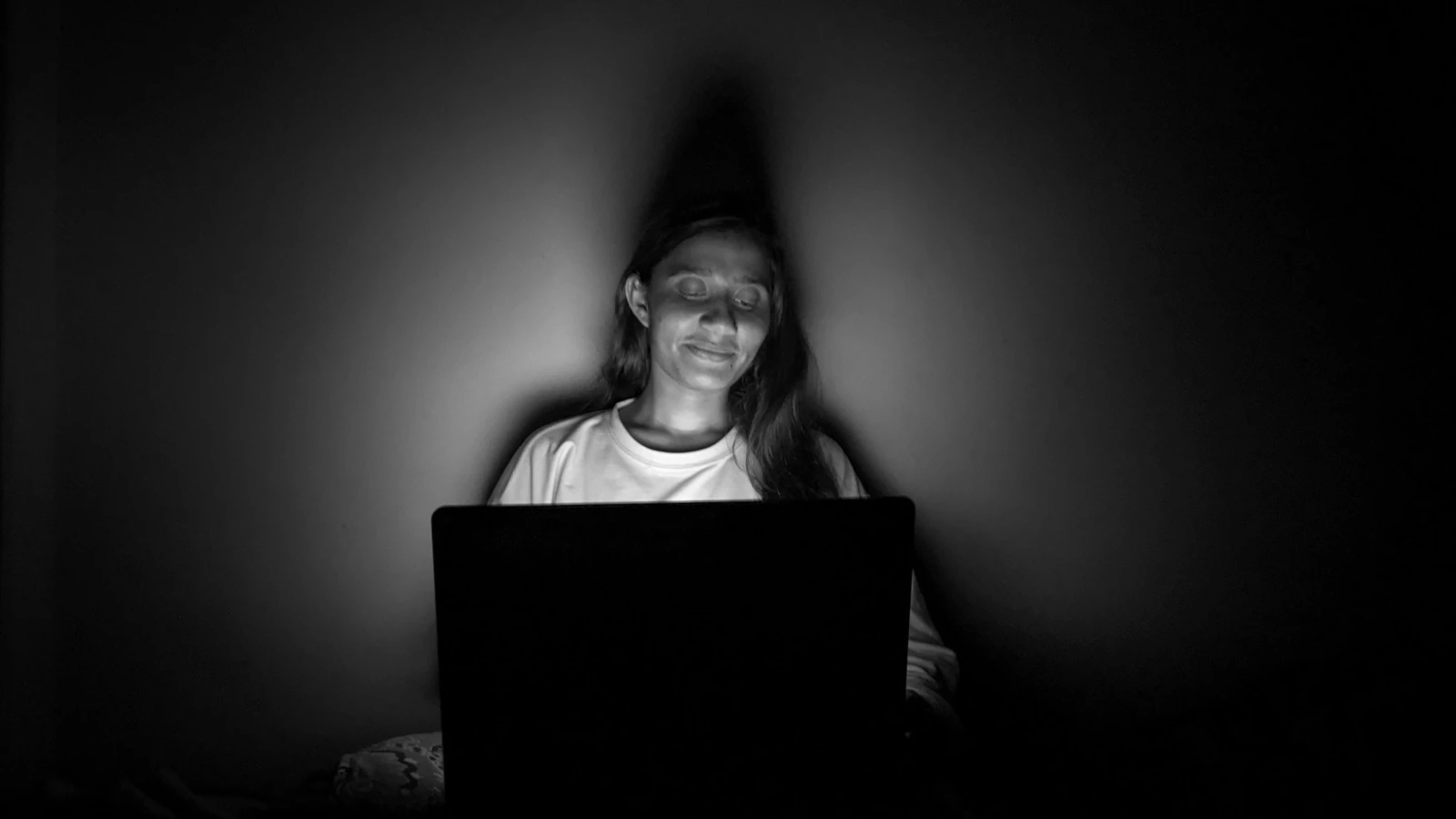 Donna seduta in una stanza buia illuminata dallo schermo di un laptop, creando un'atmosfera serena.