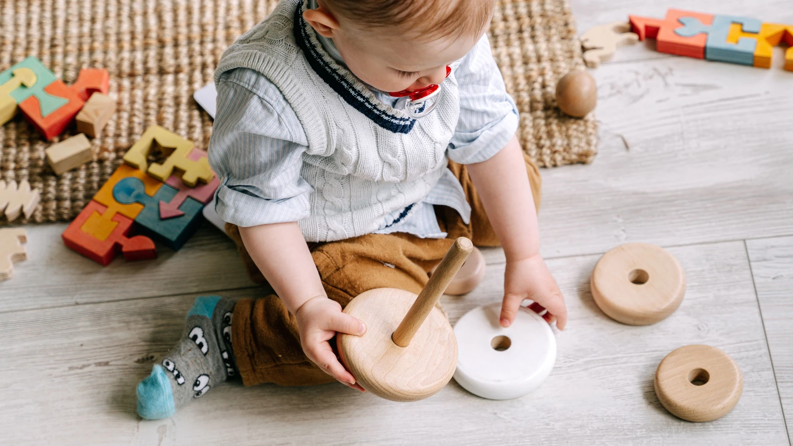 Dolce bambino che interagisce con giocattoli di legno su un tappetino da gioco, favorendo l'apprendimento e lo sviluppo precoce.