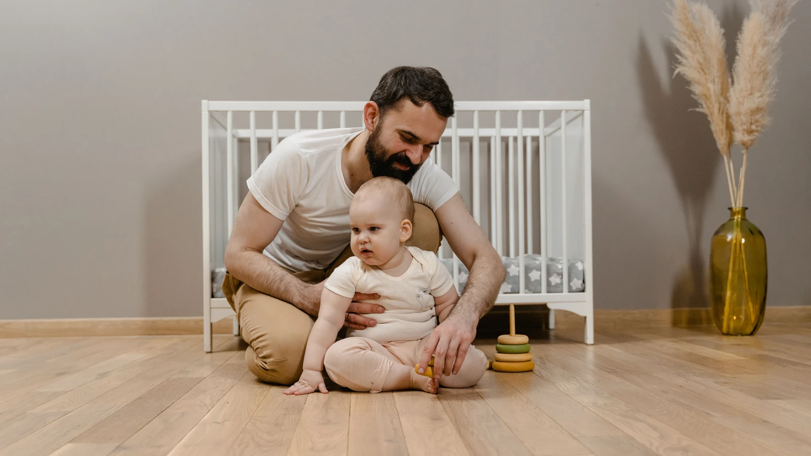Papà e bambino che condividono un momento di gioco sul pavimento in legno accanto alla culla.