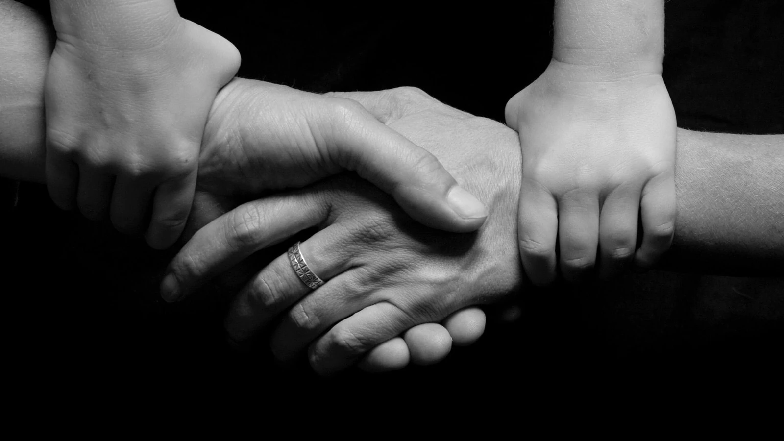 Immagine in bianco e nero di mani di un bambino e di un adulto unite, a simboleggiare fiducia e connessione.