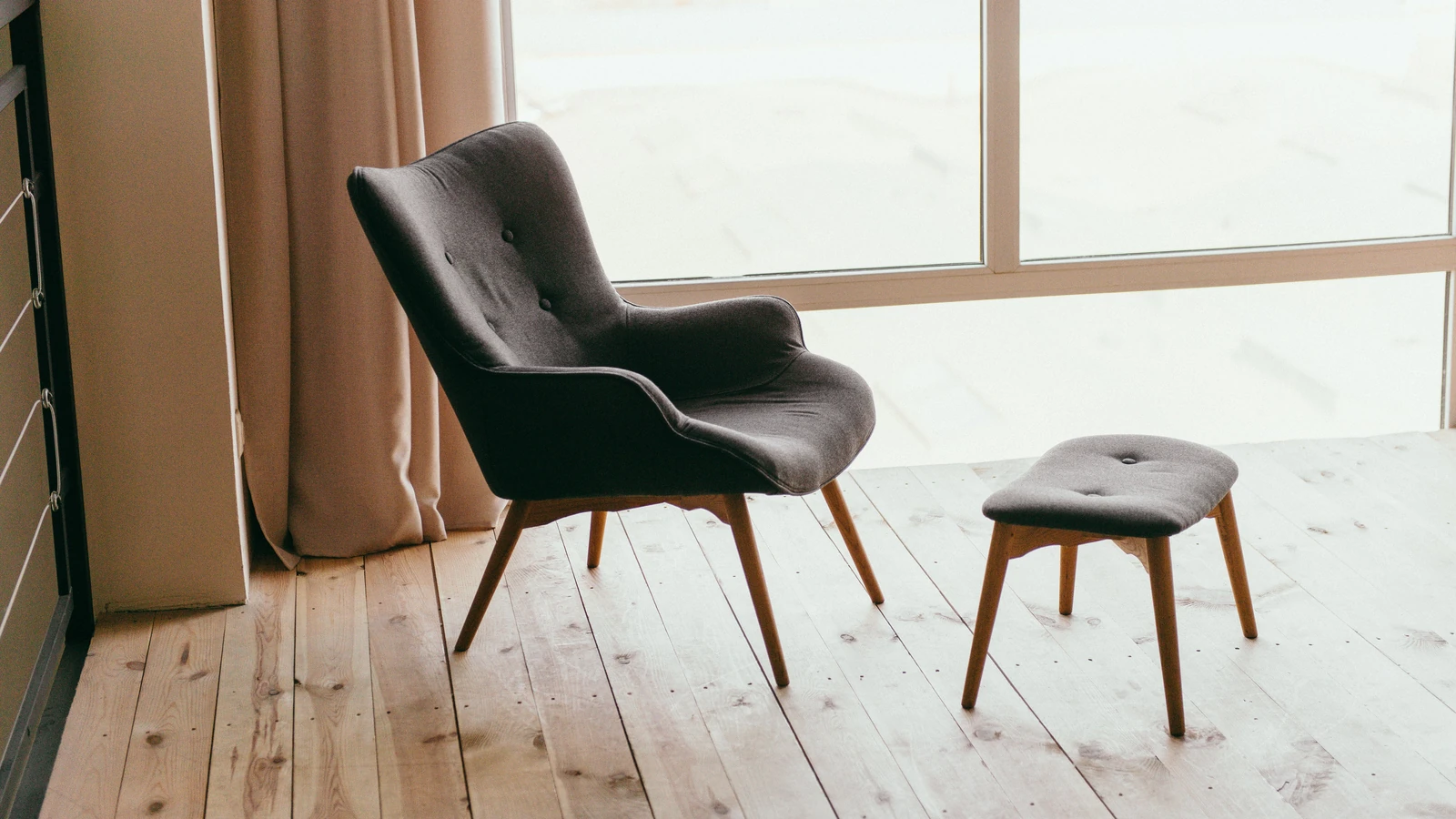 Una poltrona contemporanea e un pouf in una stanza minimalista con la luce del sole che entra da grandi finestre.