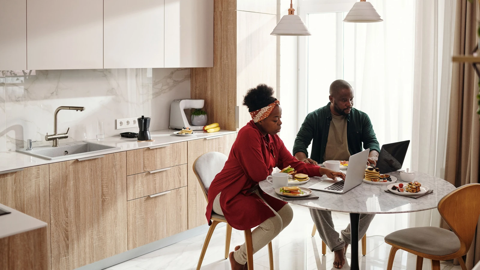 Coppia che si gode la colazione mentre usa laptop in una cucina moderna.