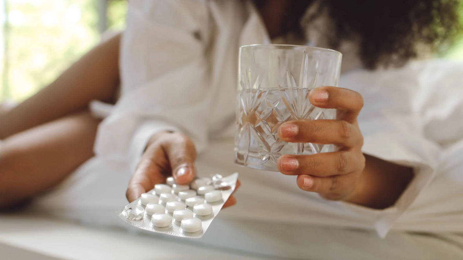 Una donna con maniche lunghe bianche tiene farmaci e un bicchiere d'acqua. Scena di vita interna. — Polina Tankilevitch – Pexels