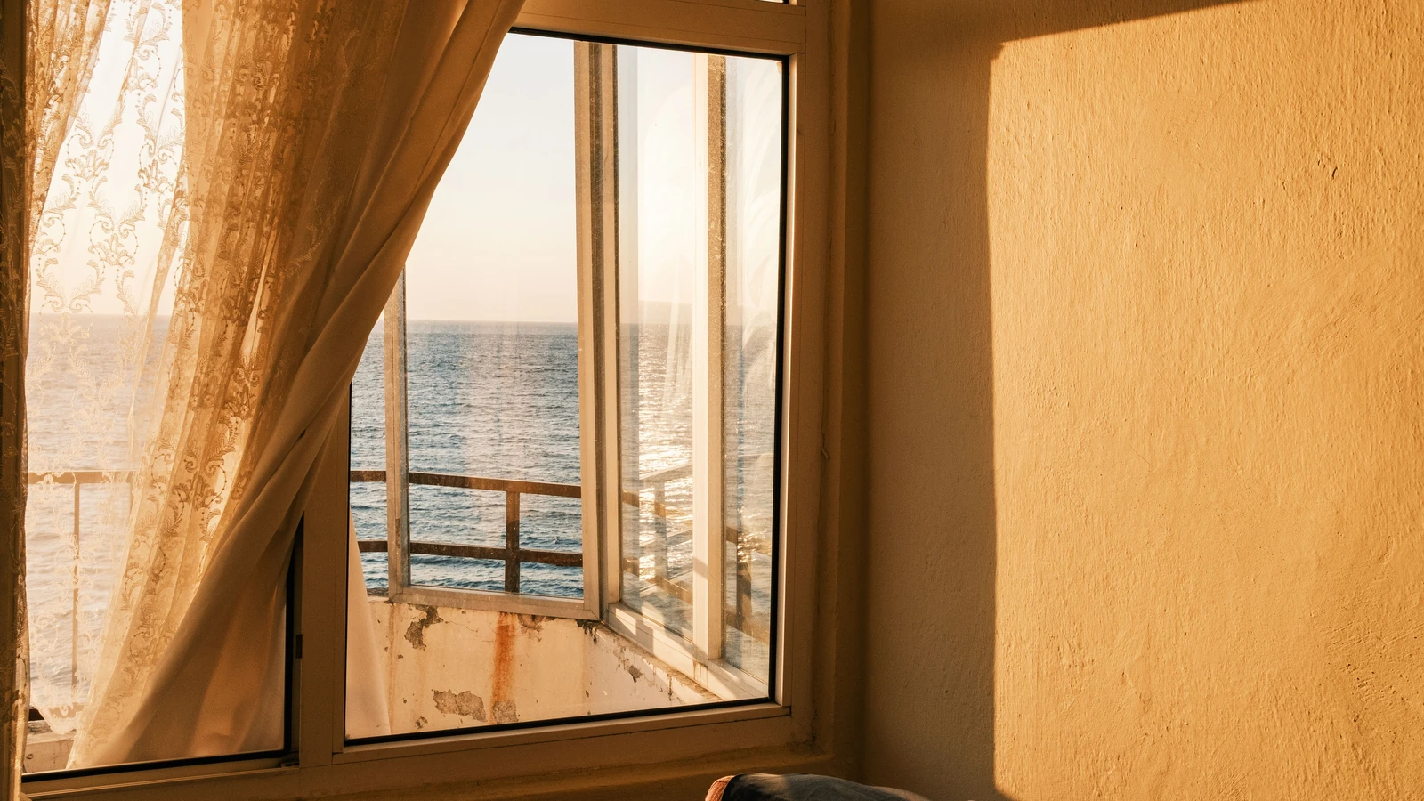 La luce solare che filtra attraverso una tenda di pizzo rivela una vista tranquilla dell'oceano, riflettendo calore e calma.