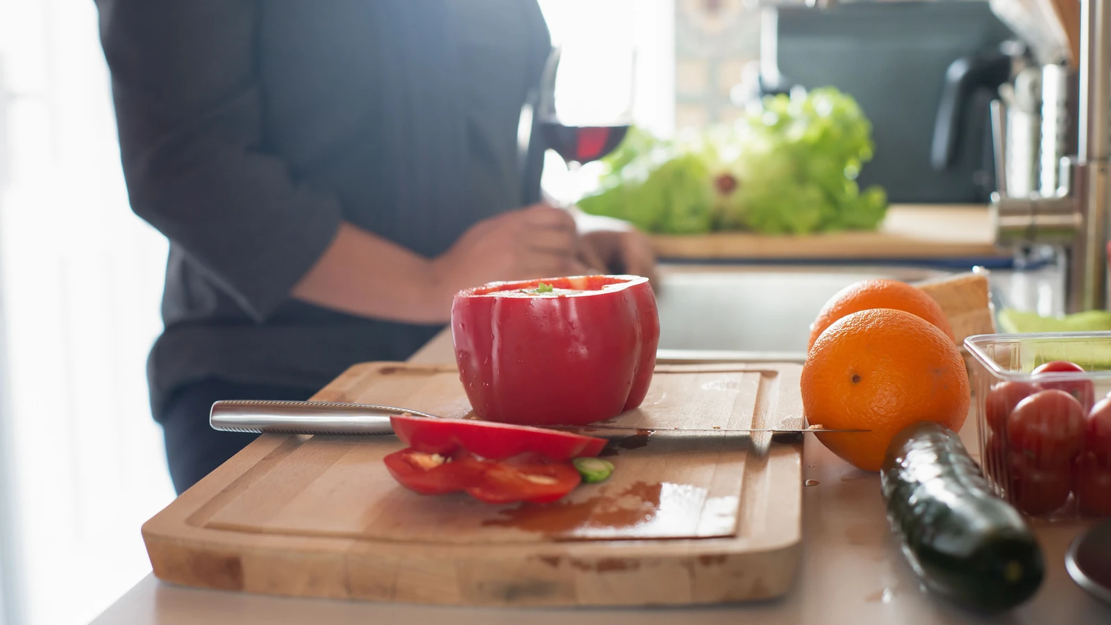 Una scena vivace di cucina con prodotti freschi, inclusi peperoni, arance e cetrioli su un tagliere di legno.