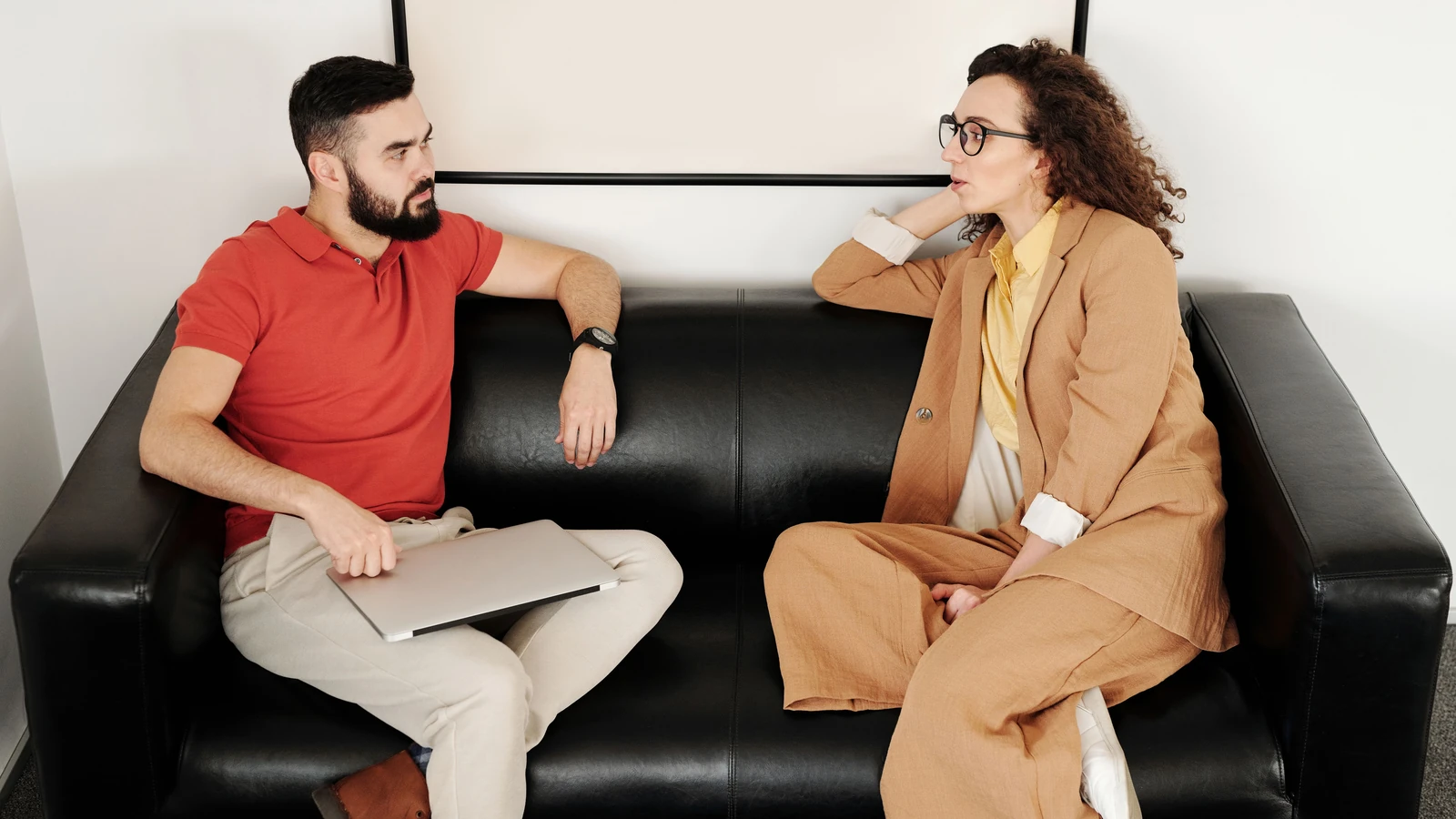 Un uomo e una donna seduti su un divano nero, che stanno avendo una conversazione professionale.