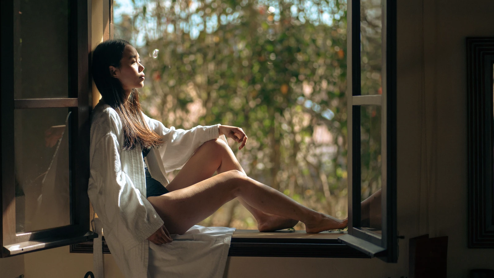 Un momento sereno di una donna in accappatoio seduta in una cornice di finestra con luce naturale che entra, catturato a Dalat, Vietnam. — Dat Tae Studio – Pexels