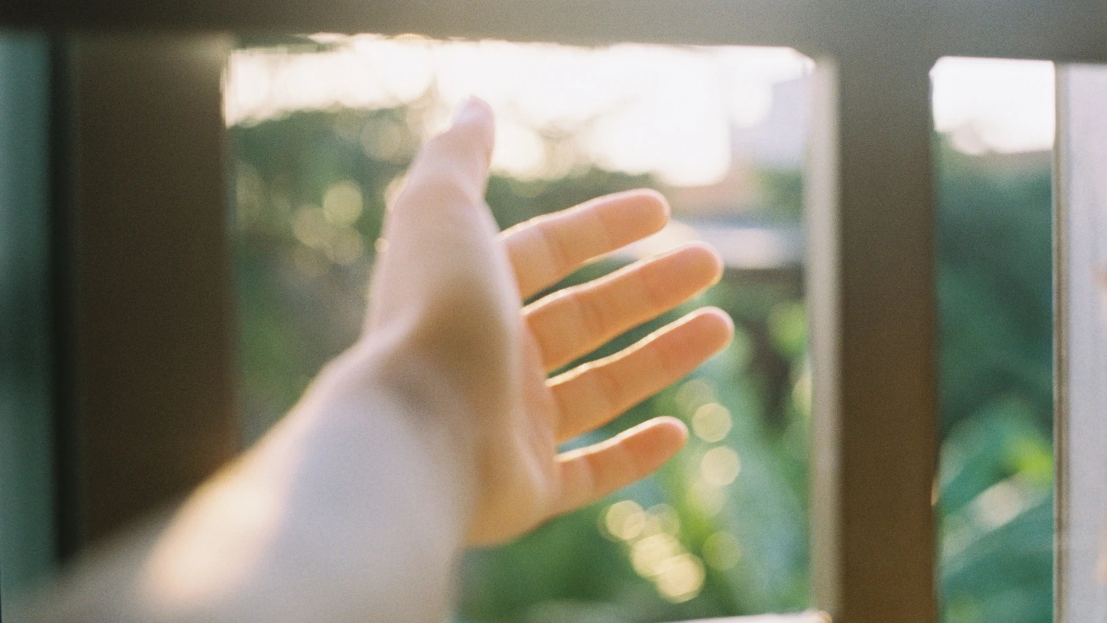 Un primo piano di una mano che raggiunge la luce del sole attraverso una finestra aperta, evocando libertà.