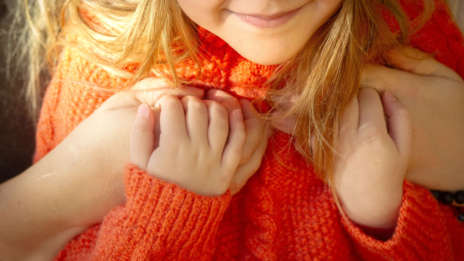 Un bambino con un maglione arancione si tiene per mano, simbolo di calore e affetto.