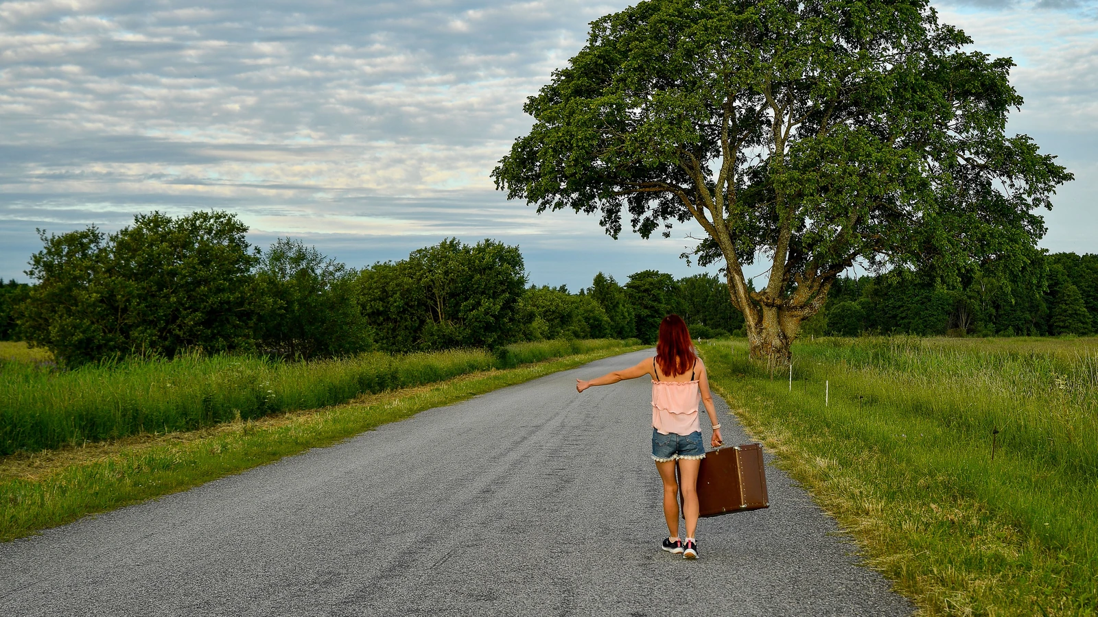Una donna fa l'autostop su una strada pittoresca a Kolga, in Estonia, immersa nel verde e con un cielo limpido. — Margo Evardson – Pexels