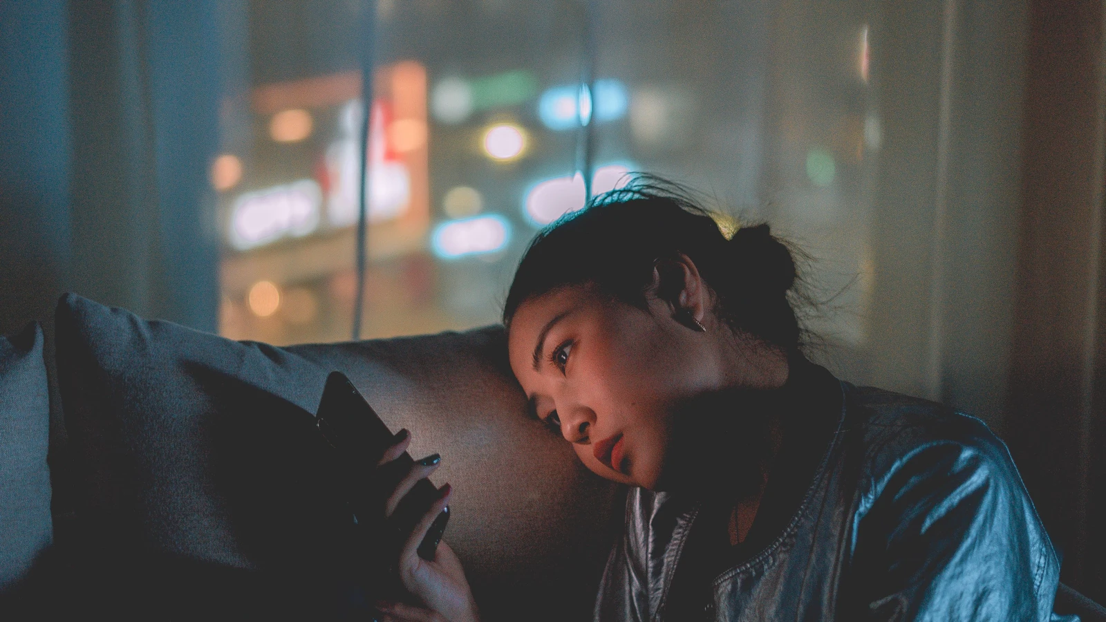 Una donna che guarda il suo telefono cellulare di notte con le luci della città sfocate sullo sfondo.