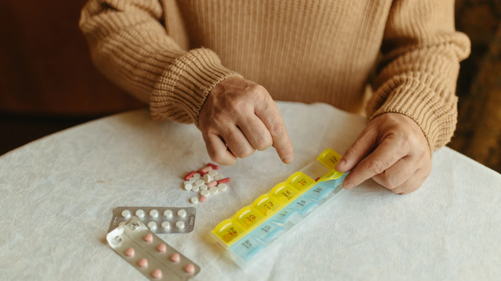 Anziano che organizza i farmaci giornalieri con un organizer settimanale di pillole su un tavolo all'interno.