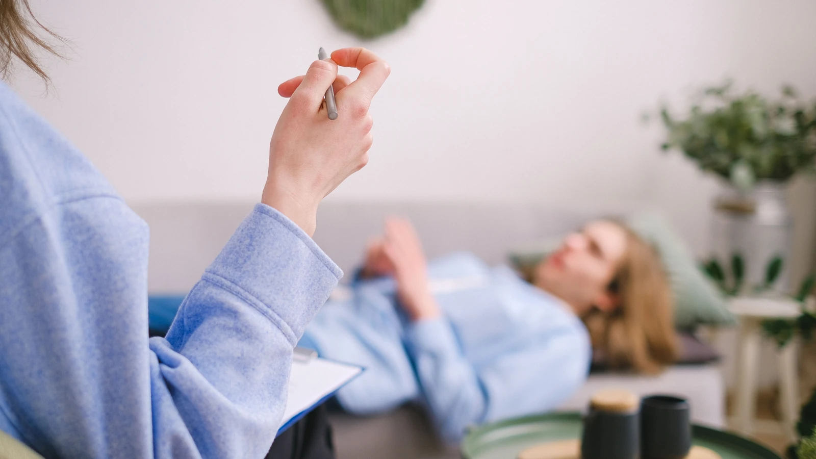 Terapeuta che prende appunti durante una seduta di terapia con un cliente rilassato sdraiato su un divano.
