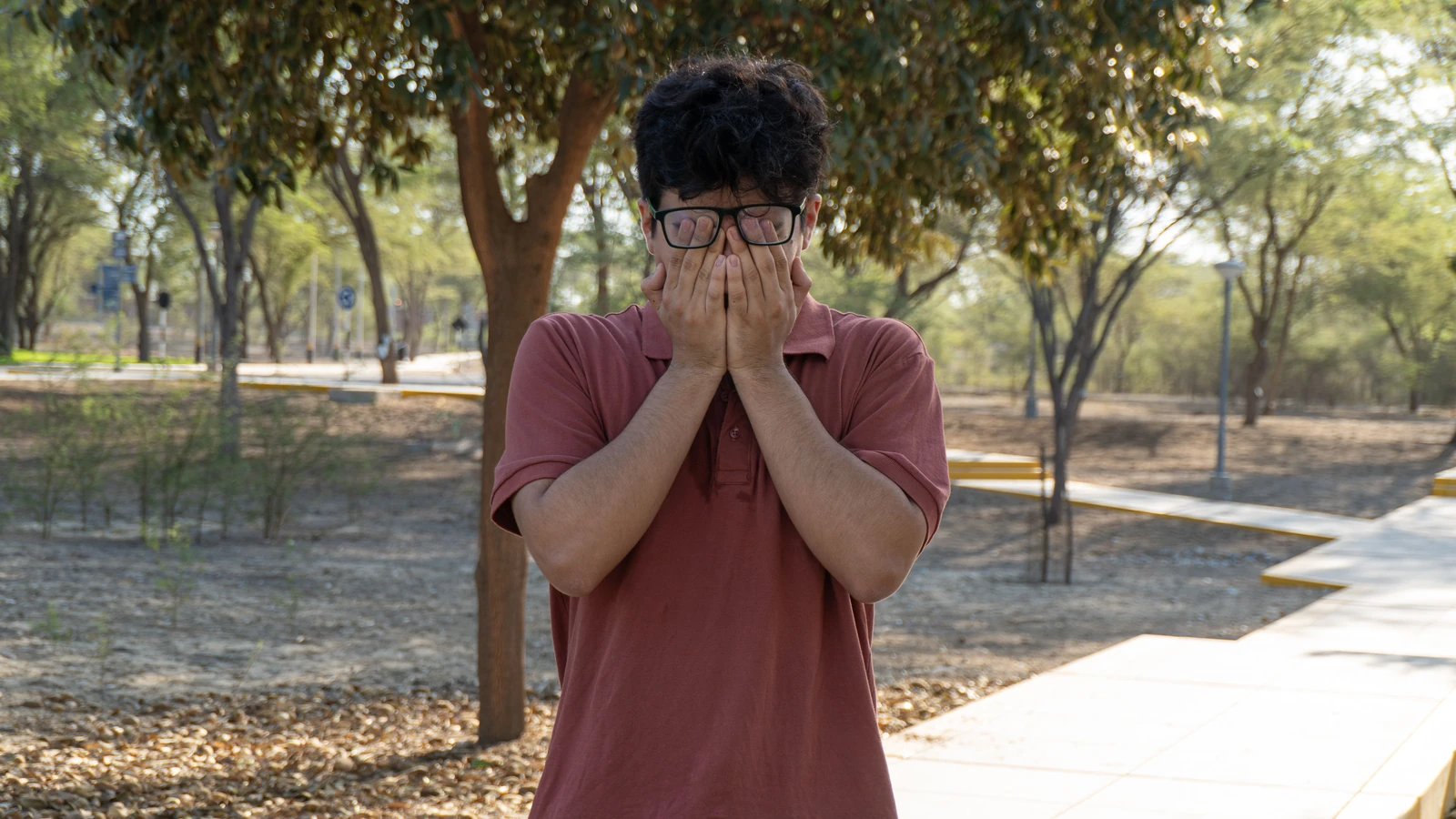 Un giovane si copre il volto in un parco, esprimendo le proprie emozioni in un paesaggio arido e sereno a Piura, in Perù.