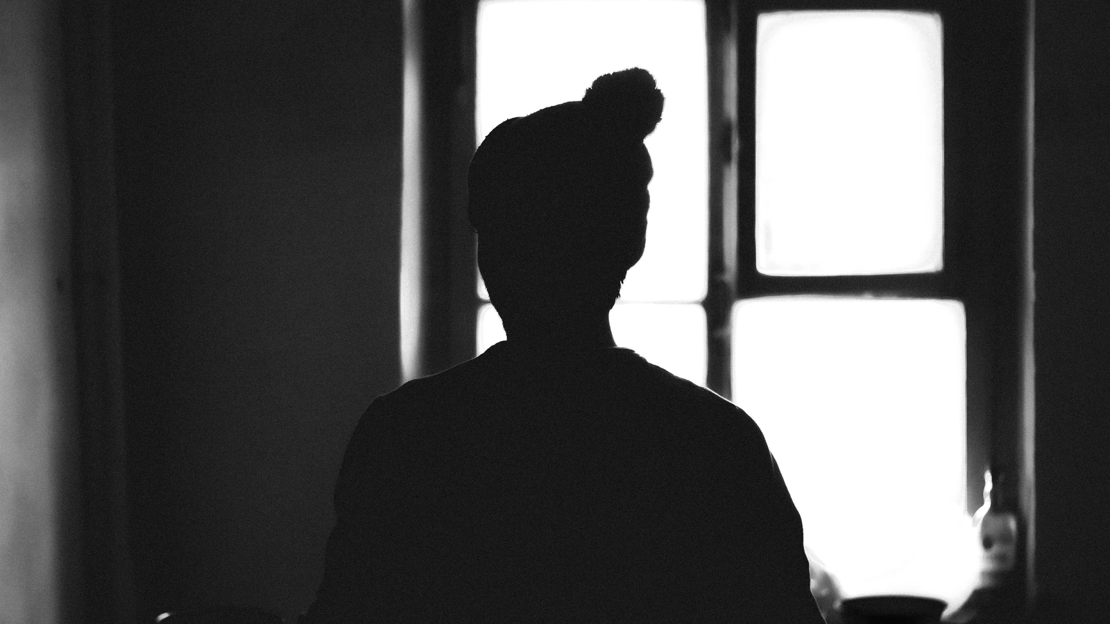 Silhouette monocromatica di una persona in piedi vicino a una finestra, creando un'atmosfera drammatica.