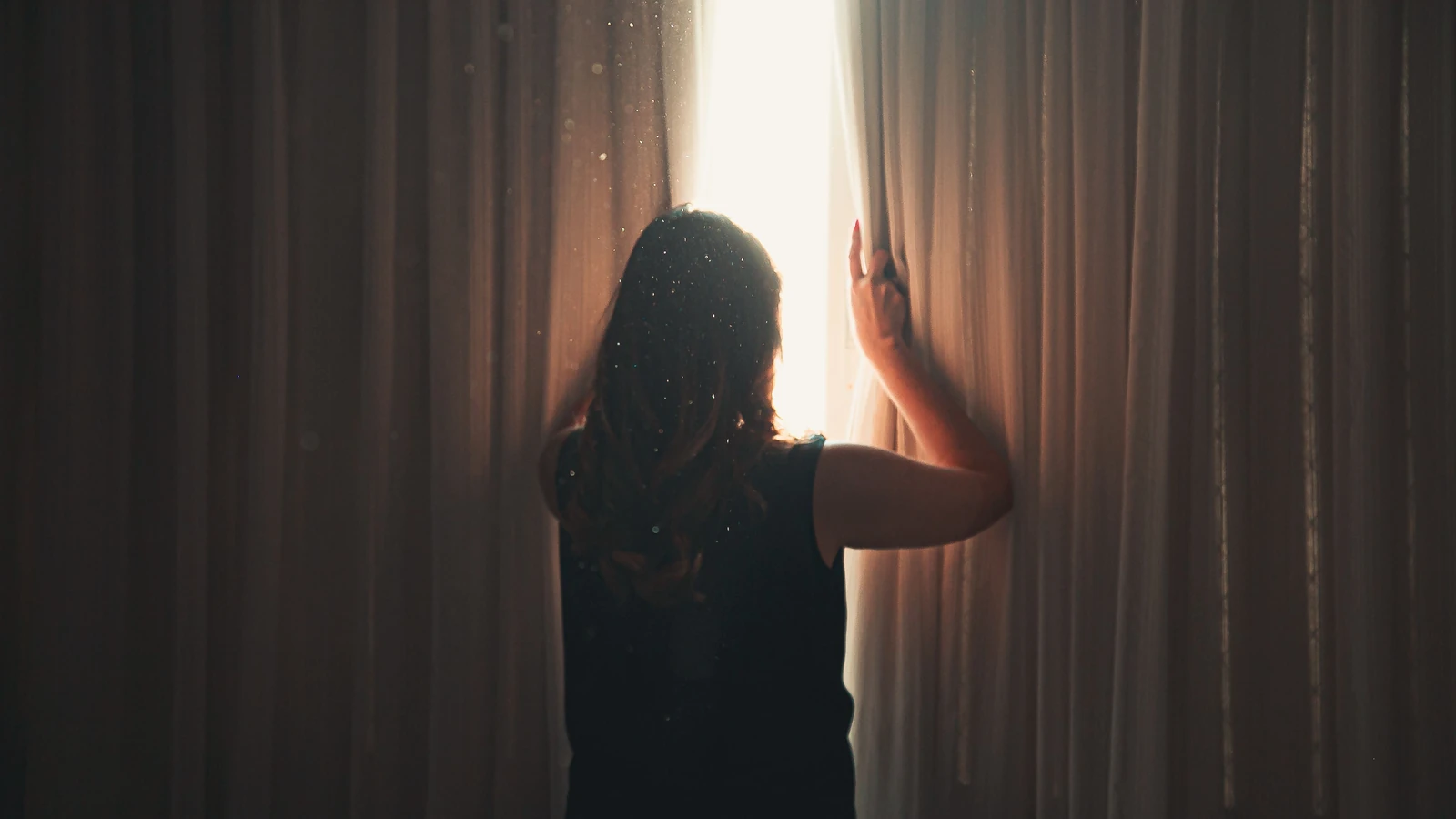 Una donna apre le tende mentre la luce del sole illumina dolcemente la stanza, creando un'atmosfera magica.
