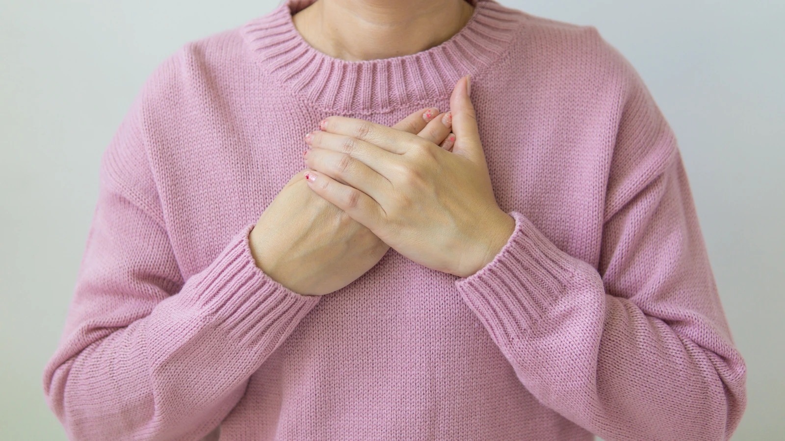 Una donna posa delicatamente le mani sul petto, indossando un morbido maglione rosa, simbolo di cura e benessere.