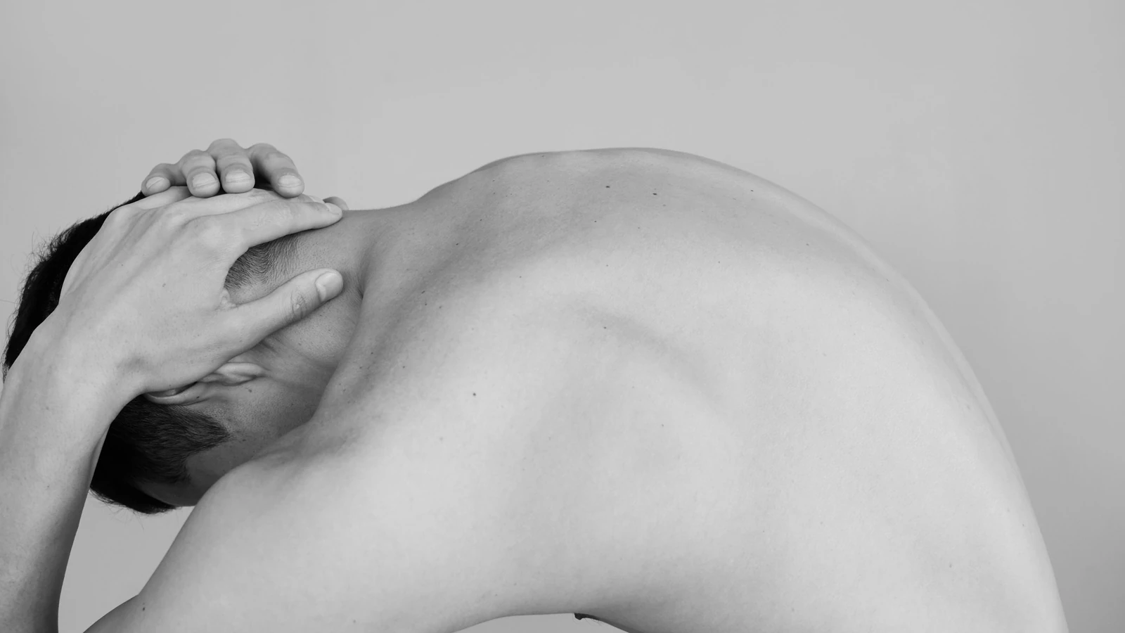 Servizio fotografico in studio in bianco e nero che cattura la postura piegata di un uomo a torso nudo, evidenziando il torso maschile.