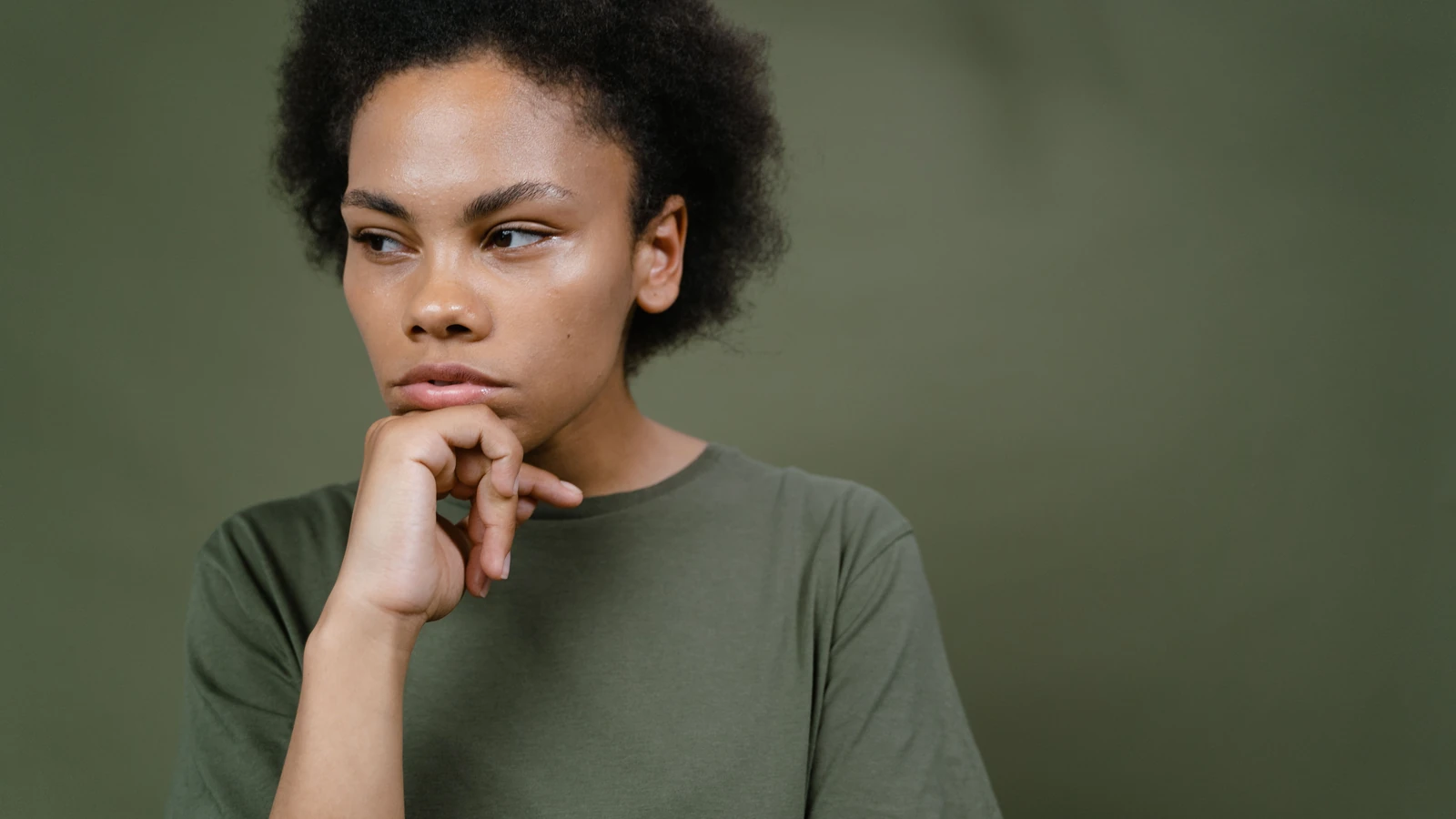 Una giovane donna pensierosa con capelli afro che contempla e guarda altrove, enfatizzando l'individualità e l'emozione.