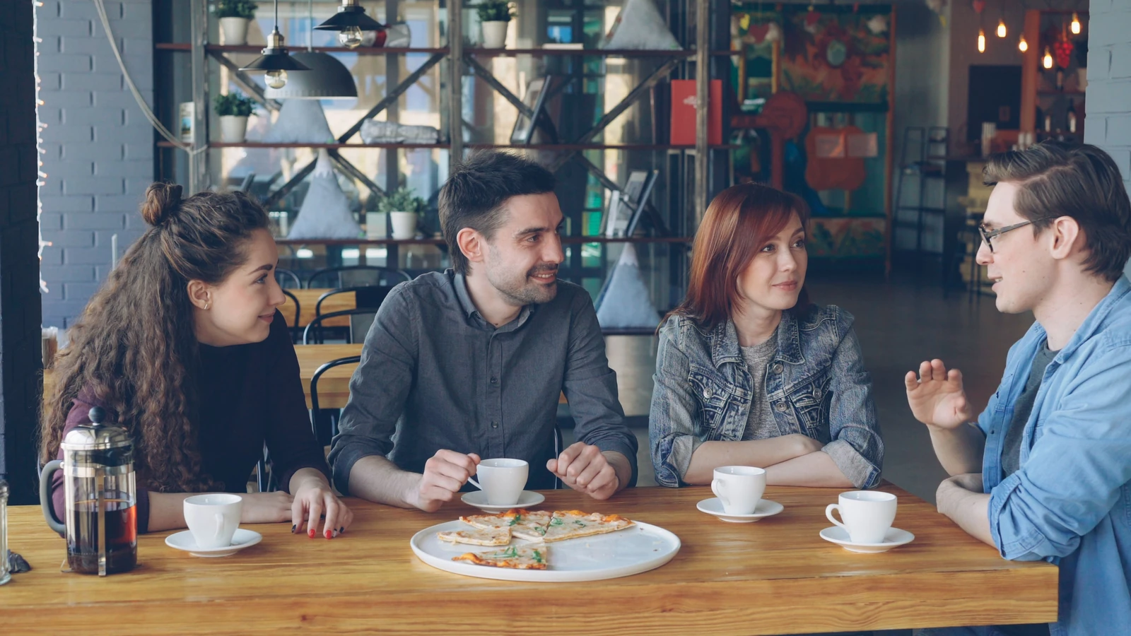 Un gruppo di giovani adulti si gode un caffè e una pizza in un bar alla moda.